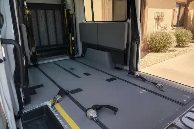 Interior of a wheelchair-accessible transport van with tie-down straps, with Phoenix, AZ desert views outside the door.
