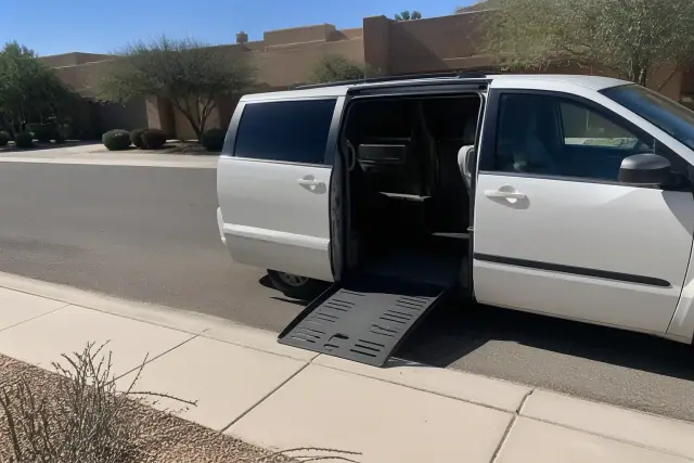 A medical transport van with an extended ramp parked at a Phoenix, AZ residence with desert landscaping.