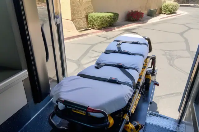 Stretcher secured with safety belts at the rear doors of a vehicle in Phoenix, AZ under bright desert sunlight.