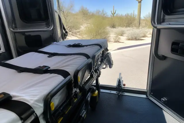 Stretcher secured at the rear doors of a medical transport vehicle in Scottsdale, AZ, with desert saguaros in the back.