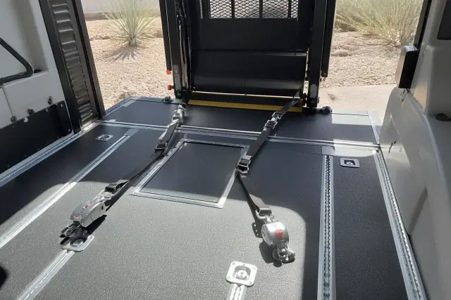 Wheelchair lift and four-point tie-down straps installed in a vehicle in Phoenix, AZ, with desert landscape visible.