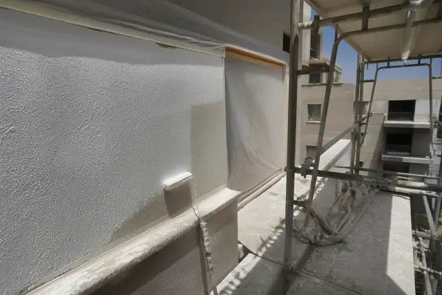 A partially painted apartment exterior wall with masking tape and metal scaffolding at a jobsite in Phoenix, AZ.