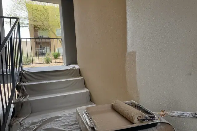 Wet paint roller on a tray in a Scottsdale, AZ apartment stairwell with drop cloths and fresh wall paint.