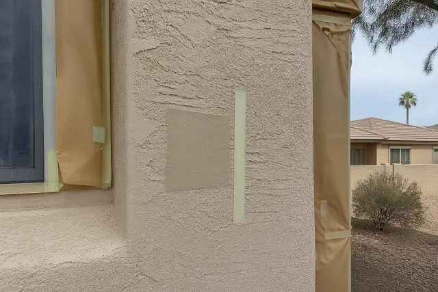 A color-matched paint sample patch and masking tape on a stucco exterior wall at a home in Phoenix, AZ.