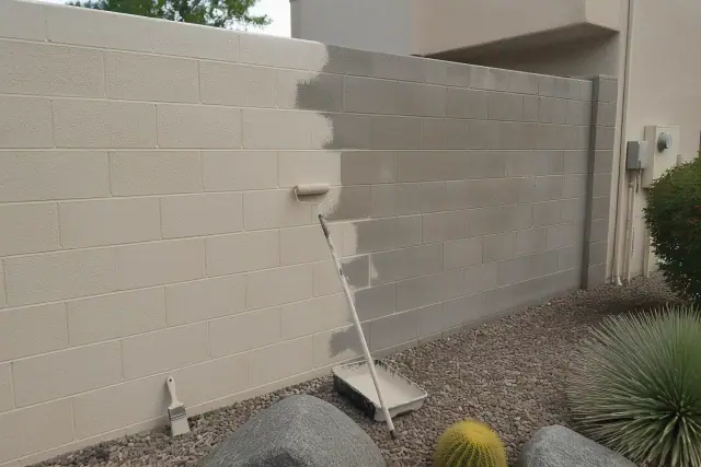 A painter working on a block wall with rollers and brushes in a residential yard in Tempe, AZ.