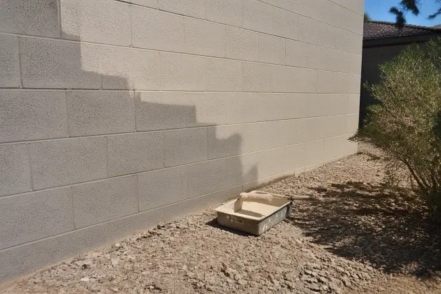 A partially painted masonry block wall at a worksite in Gilbert, AZ, with a paint tray and roller on the ground.