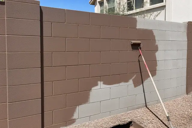 A half-finished block wall with fresh masonry coating and paint rollers at a job site in Mesa, AZ.