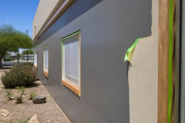 A commercial exterior wall in Peoria, AZ with fresh paint, wet brush strokes, and masking tape on a rough stucco surface.