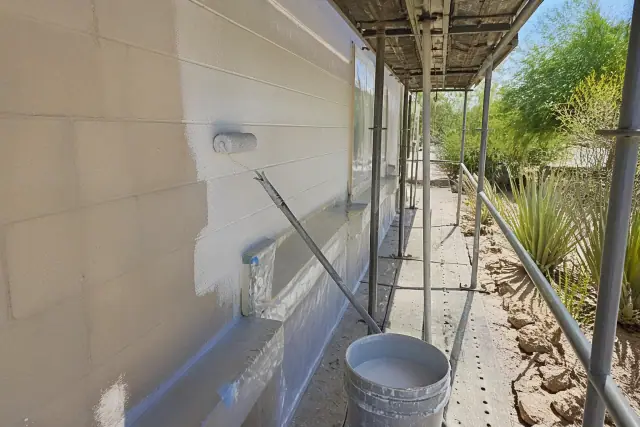 Painter applying elastomeric paint to a commercial building wall on a scaffold in Paradise Valley, AZ.