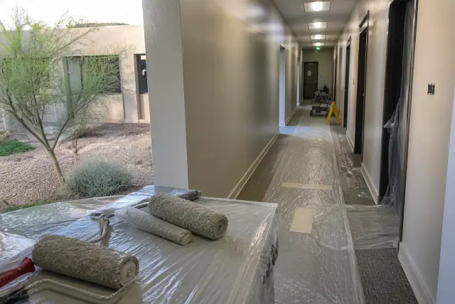 Painter applying neutral paint to a commercial office hallway in Scottsdale, AZ, with plastic-covered floors.