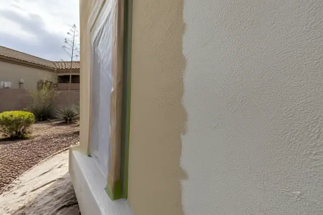 Contractor applying fresh paint to a textured stucco wall at a jobsite in Goodyear, AZ.