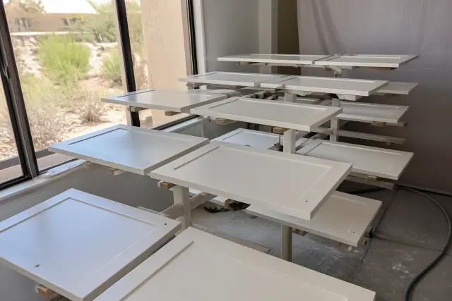 Dismantled kitchen cabinet doors on drying racks at a workspace in Phoenix, AZ, with a view of desert landscaping.