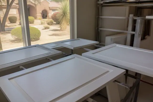 Cabinet doors drying on racks in a Phoenix, AZ workshop with a view of xeriscape landscaping through a window.