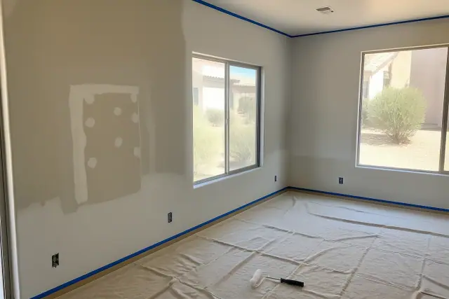 Drywall patch and freshly painted wall in a Glendale, AZ home with taped trim and painting supplies on a drop cloth.