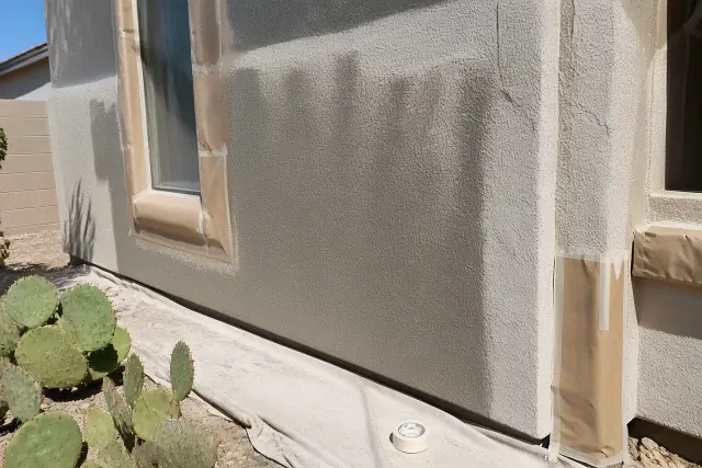 Exterior painting in progress on a stucco wall with masking paper and prickly pear cacti in Glendale, AZ.