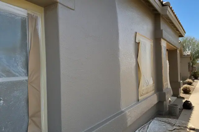 A worker applying fresh paint to a textured stucco residential wall in Surprise, AZ.