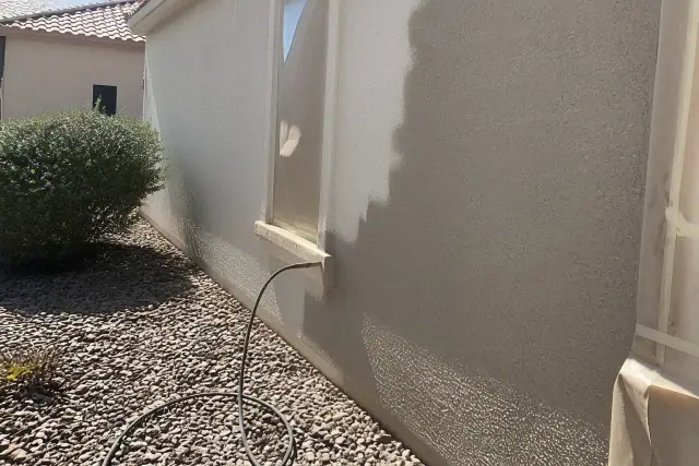 Paint sprayer hose and masked window on a stucco wall during a home exterior painting project in Goodyear, AZ.