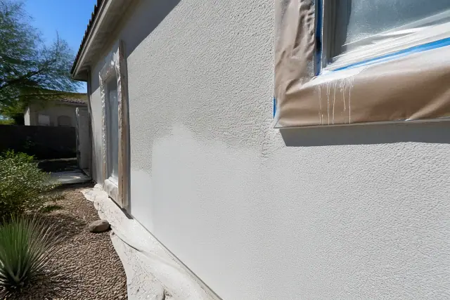 Painter applying wet paint to a stucco wall with protective masking paper at a home in Mesa, AZ.
