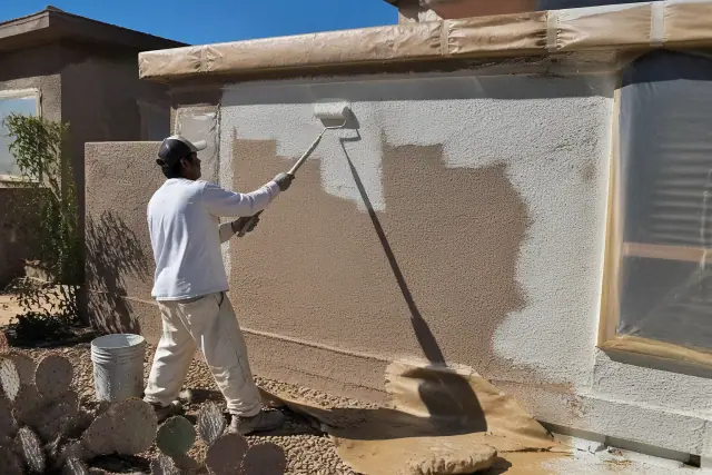 Painter applying fresh paint to a rough stucco wall at a residential home in Scottsdale, AZ.