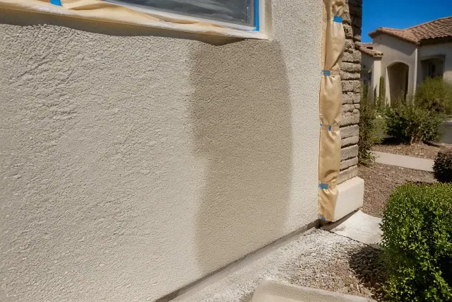 Wet paint being applied to a rough stucco wall at an exterior painting jobsite in Tempe, AZ.