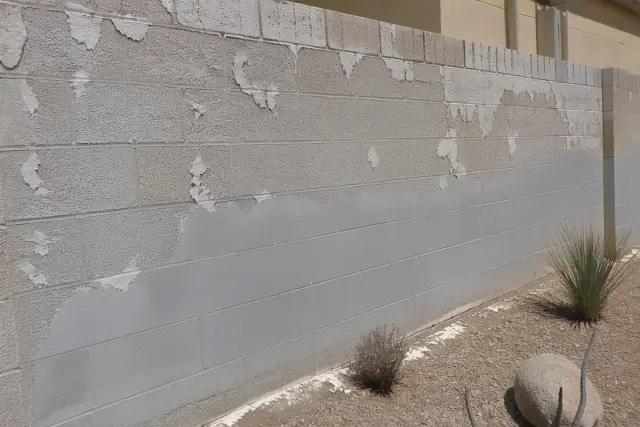 A contractor repainting a weathered concrete block wall with flaking paint in Phoenix, AZ.