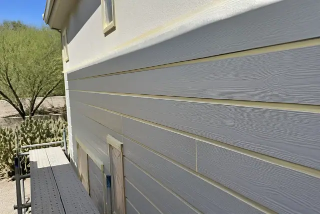 Fiber cement siding with masking tape prep on a building exterior in Phoenix, AZ, with prickly pear cacti in the background.