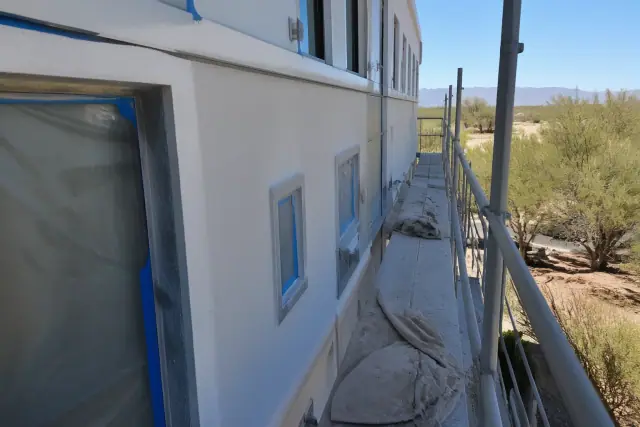 A high-rise commercial building under exterior painting in Phoenix, AZ, with scaffolding, drop cloths, and masking tape.