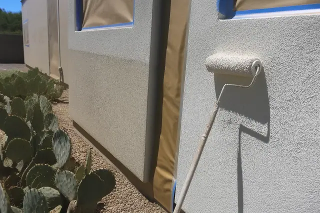 A paint-stained roller rests against a partially masked stucco wall in a sunny Goodyear, AZ backyard.