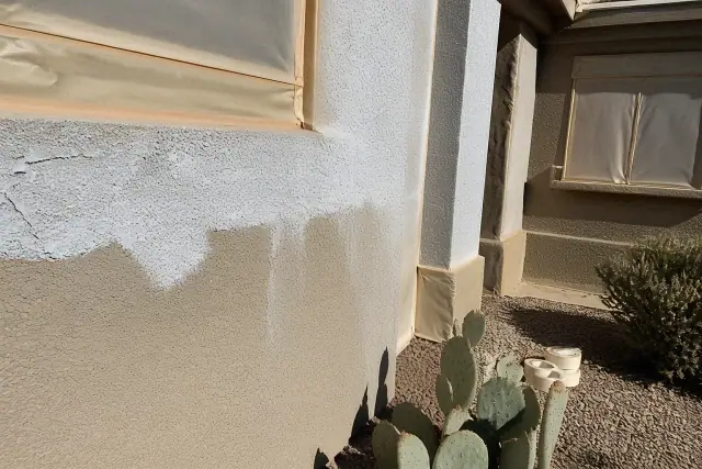 Worker applying primer to a stucco wall with masking tape and desert xeriscaping in Glendale, AZ.