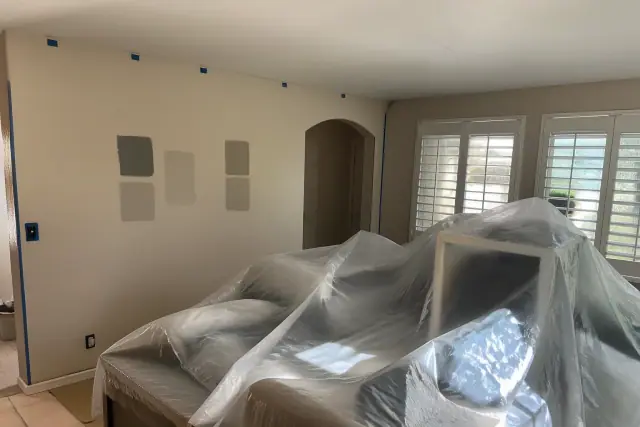 Residential room undergoing renovation with paint swatches on walls and furniture covered in plastic in Phoenix, AZ.