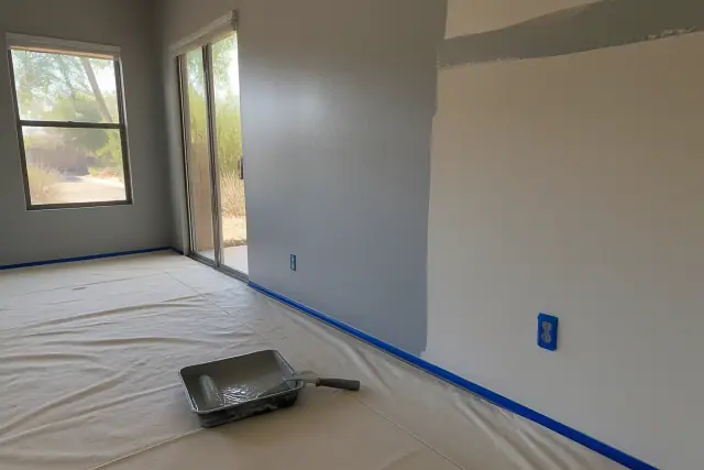 Freshly painted living room walls with tape on trim and a paint roller in a tray at a residence in Tempe, AZ.
