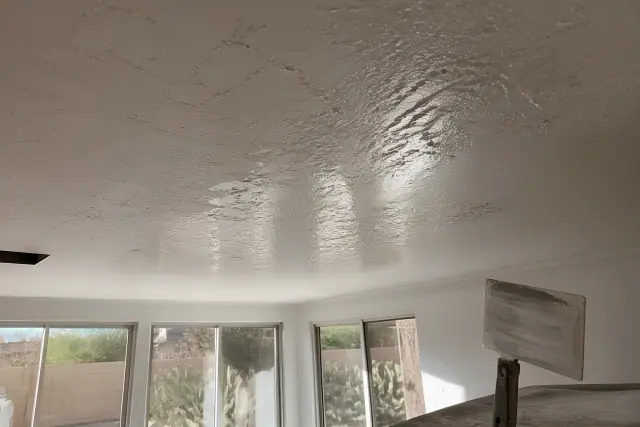 Knockdown texture ceiling repair with wet drywall compound and a knife in a Phoenix, AZ home with cacti outside.