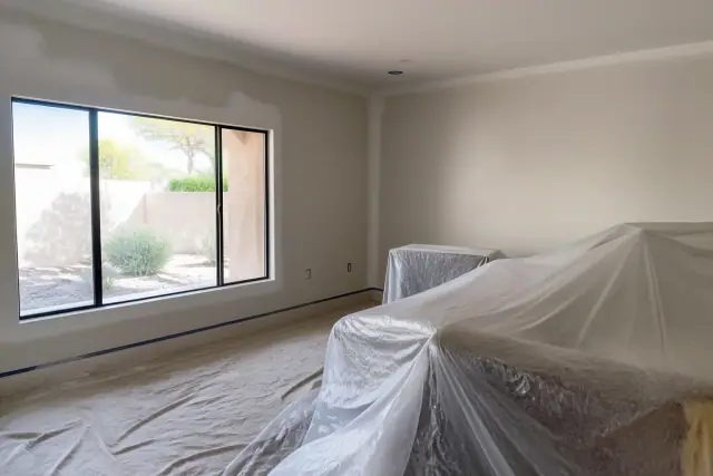 Freshly painted walls with plastic masking and drop cloths in a Phoenix, AZ interior with views of desert landscaping.