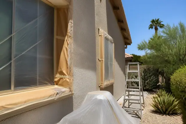 Exterior wall of a Phoenix, AZ home undergoing painting with protective masking paper around window frames.