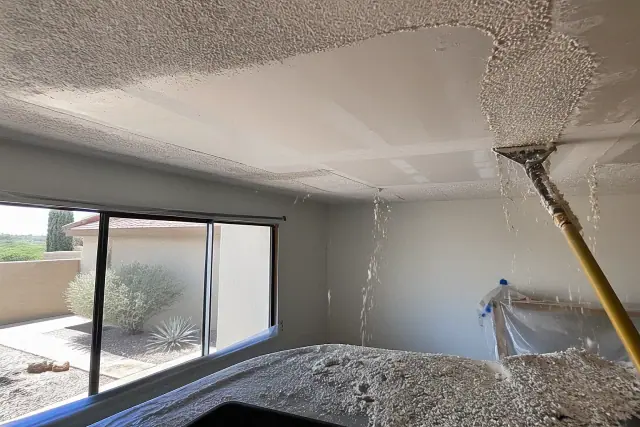 Contractor removing popcorn ceiling texture with debris on drop cloths in a Phoenix, AZ home.