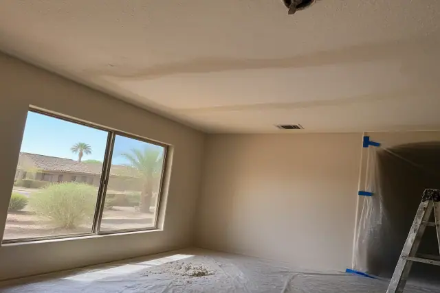 Popcorn ceiling removal progress in a Gilbert, AZ home with drywall debris on a floor sheet and desert views through a
