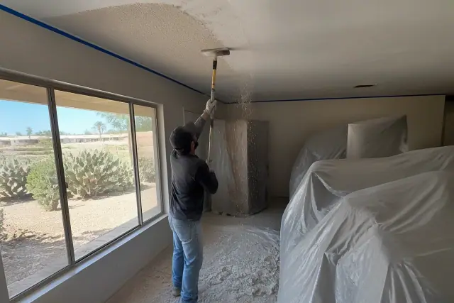 Popcorn ceiling removal in a residential room with furniture covered by plastic sheeting in Glendale, AZ.
