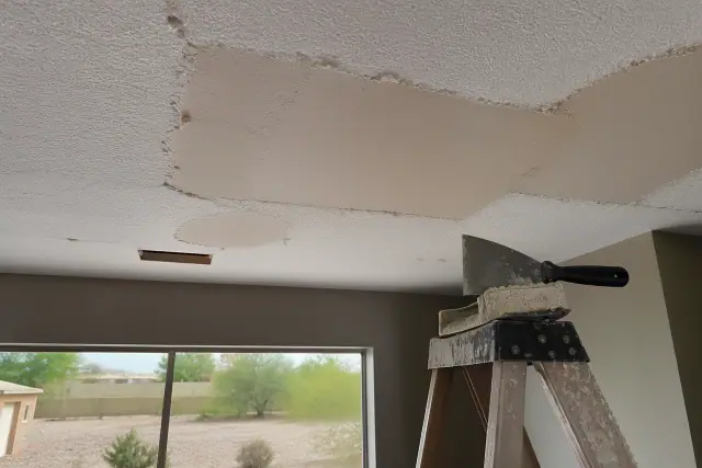 Drywall scraper on a ladder near a popcorn ceiling removal project in a residential interior in Goodyear, AZ.