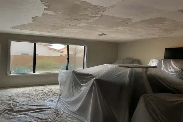 Popcorn ceiling removal in a residential room with furniture covered in plastic sheeting in Tempe, AZ.