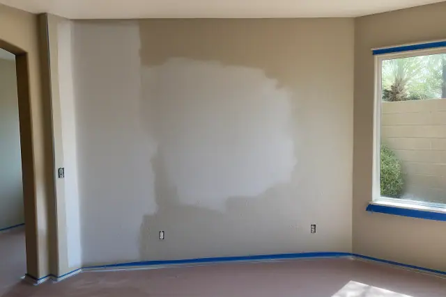 Primer coverage on a drywall patch in a residential living room in Phoenix, AZ, with taped trim and natural light.