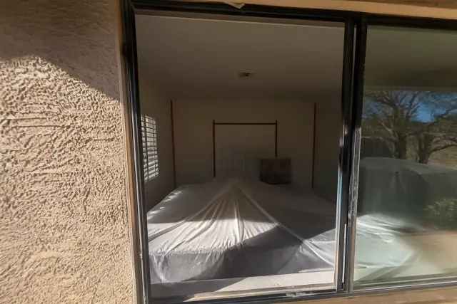 Residential room in Phoenix, AZ with furniture covered in plastic sheeting for wet scraping containment.