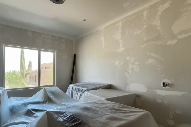 Scraped drywall in a Phoenix, AZ home with furniture covered in plastic sheeting for skim coat preparation.