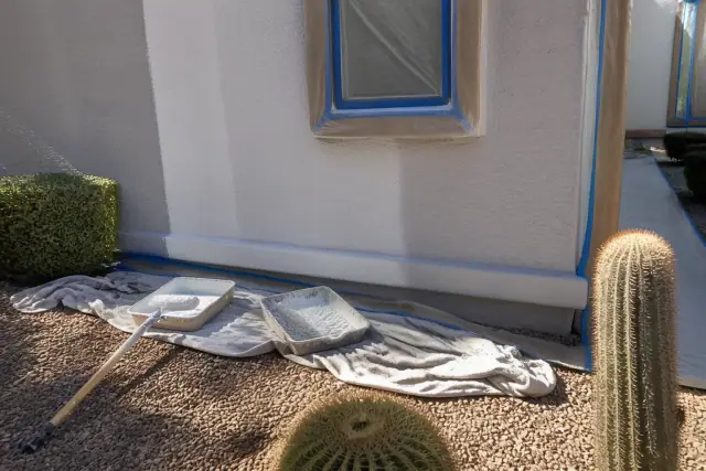 Stucco wall being painted near a window with rollers and supplies on a worksite in Phoenix, AZ.