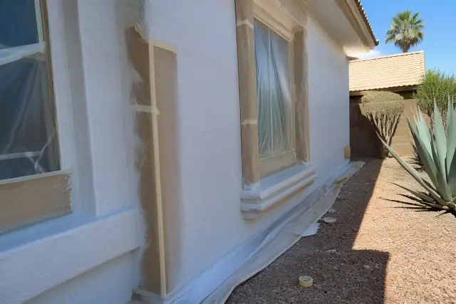 Worker applying elastomeric coating to a residential stucco wall during a home painting project in Phoenix, AZ.