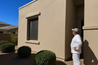 Technician inspecting a freshly painted stucco exterior wall with desert xeriscaping at a home in Phoenix, AZ.