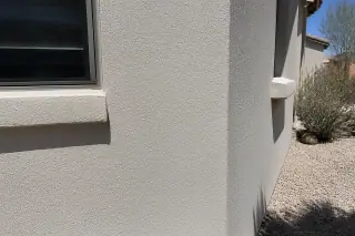 Freshly painted rough stucco wall under harsh midday sun with desert landscaping in Phoenix, AZ.