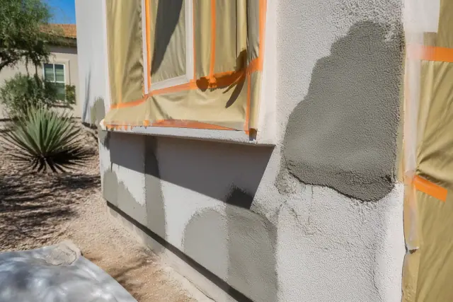 Stucco wall repair with fresh mortar infill on a home in Phoenix, AZ with xeriscaped landscaping in the background.