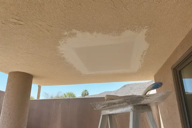A sanded drywall repair on a textured ceiling with a hawk and trowel on a ladder at a job site in Phoenix, AZ.