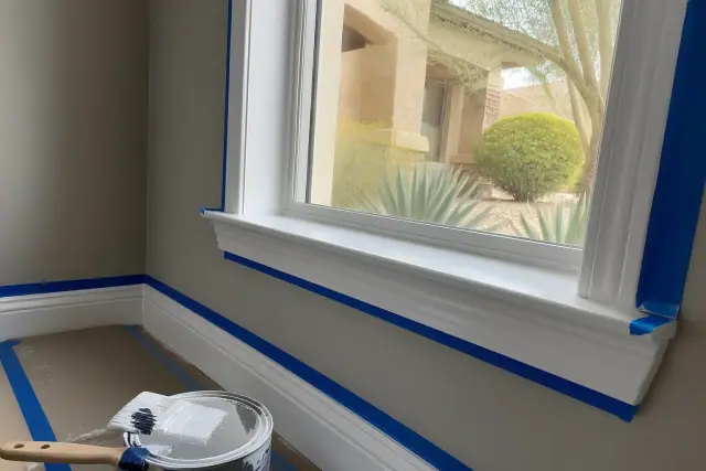 Baseboards and window casings with blue painter tape during interior trim painting in a Phoenix, AZ home.