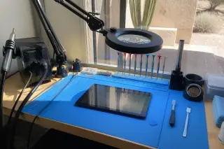 Reassembled Android tablet on a workbench with a soldering station and desert sunlight in Phoenix, AZ.